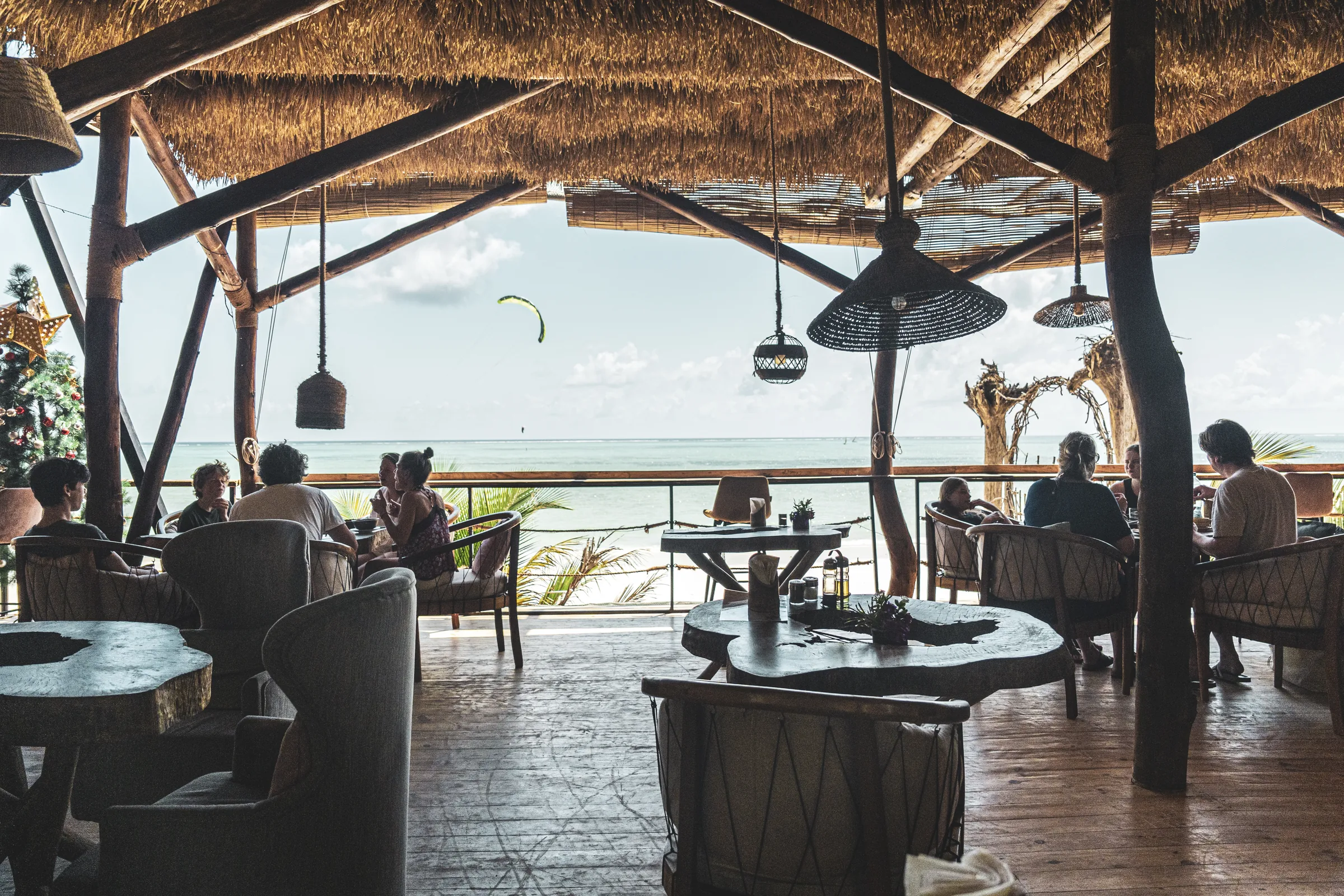 El restaurante del Nest sobre la playa con una cometa cruzando el horizonte — la escuela vive donde pasa el desayuno